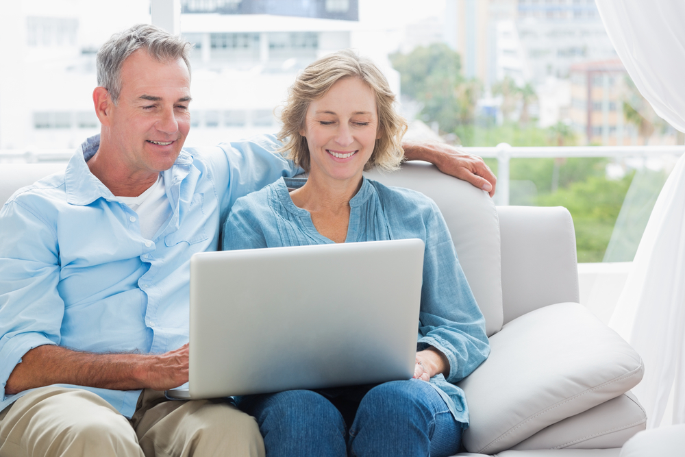 Cheerful couple relaxing on their couch using the laptop at home in the sitting room